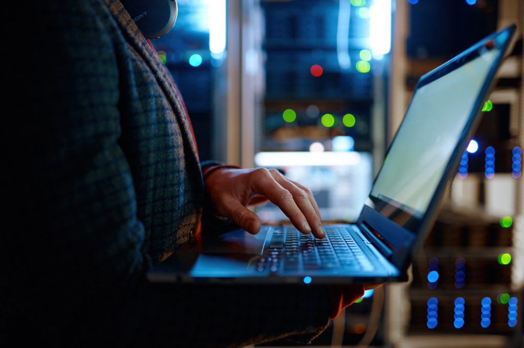 IT support specialist using a laptop to monitor servers and network performance in a modern data centre environment
